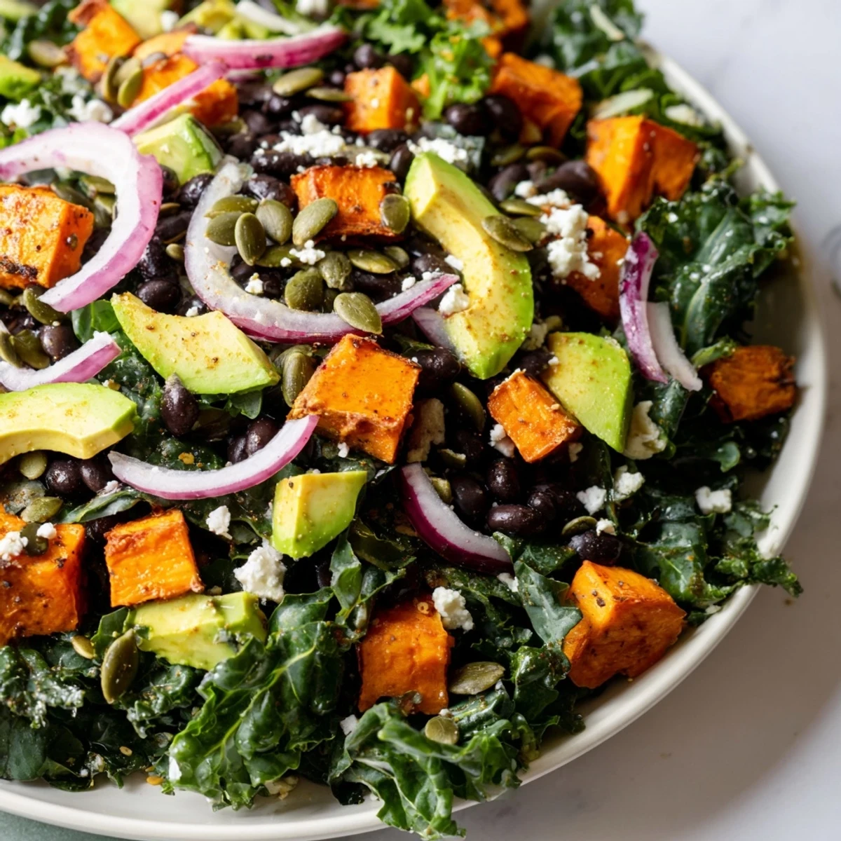A colorful bowl of massaged kale salad, featuring tender sweet potato and creamy avocado.