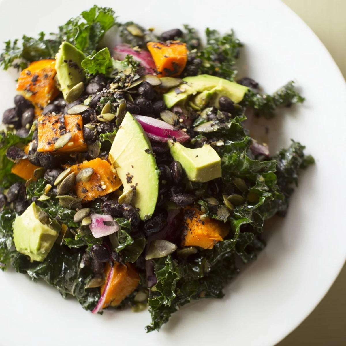 Fresh, bright massaged kale salad with black beans, sweet potato, and avocado, ready to serve.