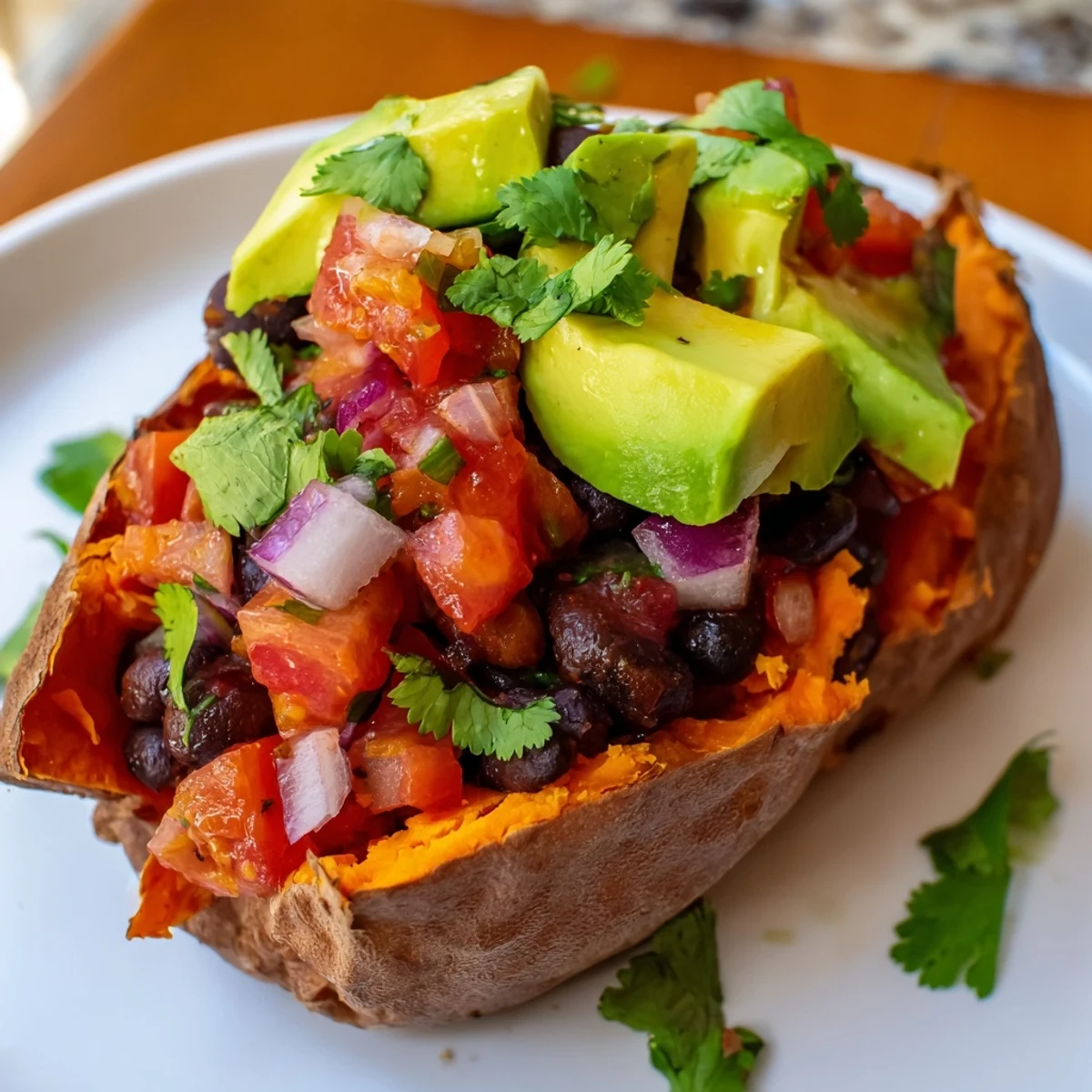 Roasted sweet potatoes topped with smoky chipotle black beans and fresh zesty tomato salsa on a rustic plate.  