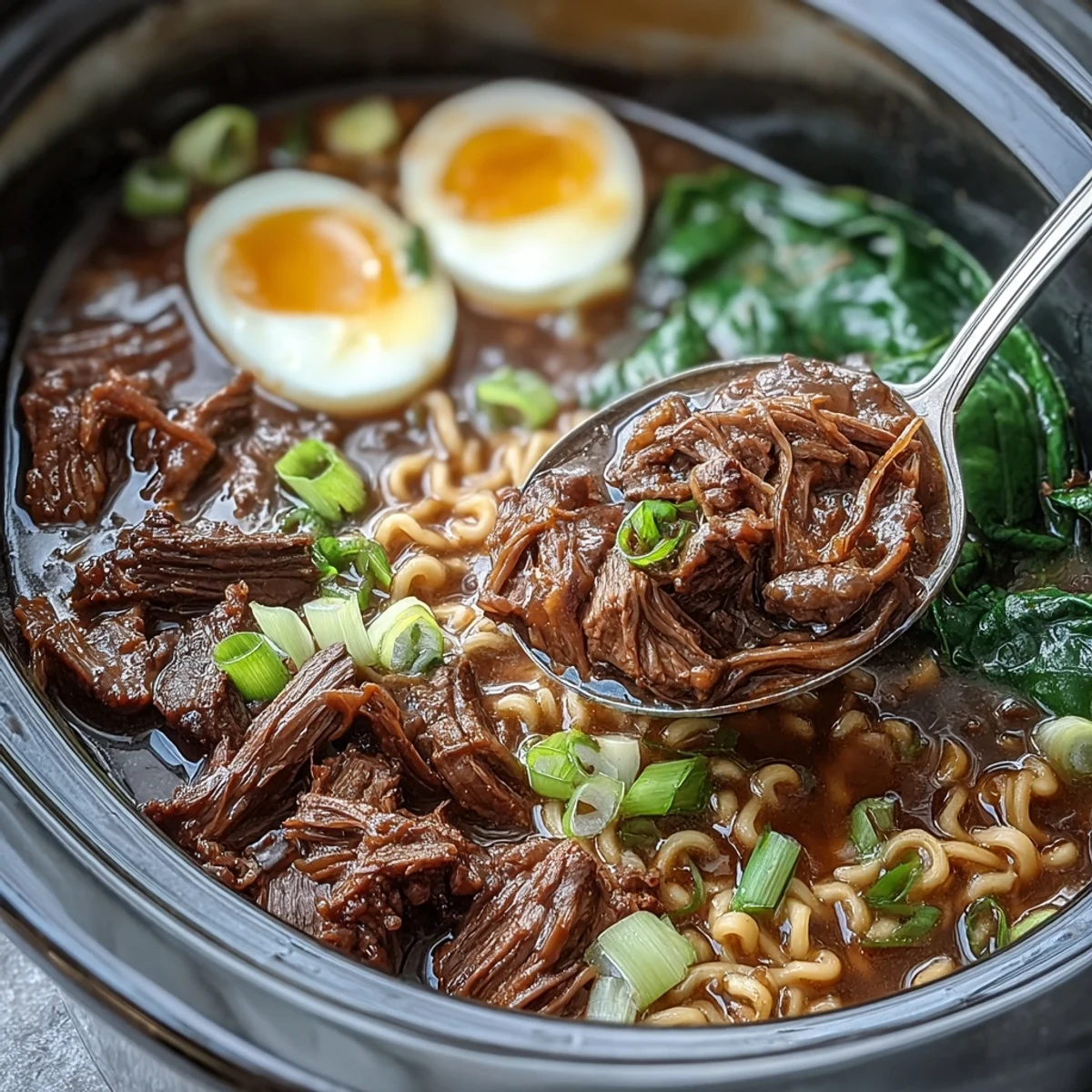 A close-up photo of Slow Cooker Beef Ramen Noodles in a rustic ceramic bowl, featuring tender shredded beef and chewy noodles in a rich, savory broth topped with sliced green onions.