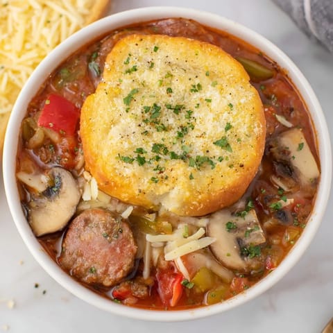 A close-up of Pizza Pot Pie Soup, showcasing bubbly cheese and a golden crusty top.
