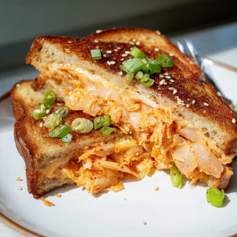 A close-up of a bubbling, cheesy Skillet Kimchi & Cheddar Fusion Grilled Cheese sandwich, sliced nearly in half.