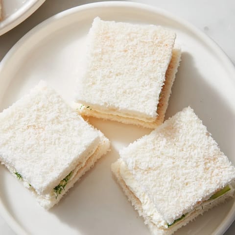 Close-up of freshly made Snowball Tea Sandwich Bites, creamy filling peeking through shredded coconut.