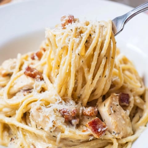 Shredded chicken and al dente spaghetti in a glossy egg-Parmesan sauce, topped with black pepper and parsley.