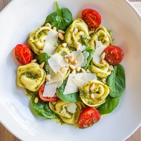 Sunlight highlights the glossy pesto coating cheese tortellini, cherry tomatoes, and spinach in this refreshing Pesto Tortellini Salad.