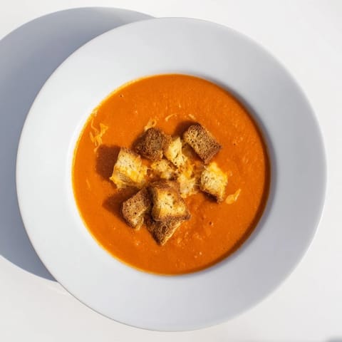 A warm bowl of roasted tomato soup with bubbly cheddar croutons.
