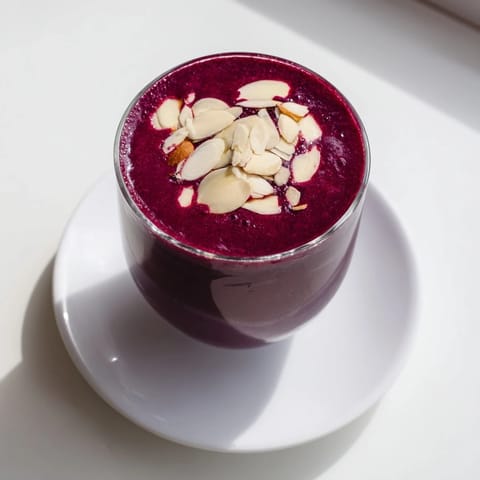 Two servings of vibrant Cherry Almond Smoothie beside a bowl of fresh cherries, a breakfast-ready blend with almond butter swirls.