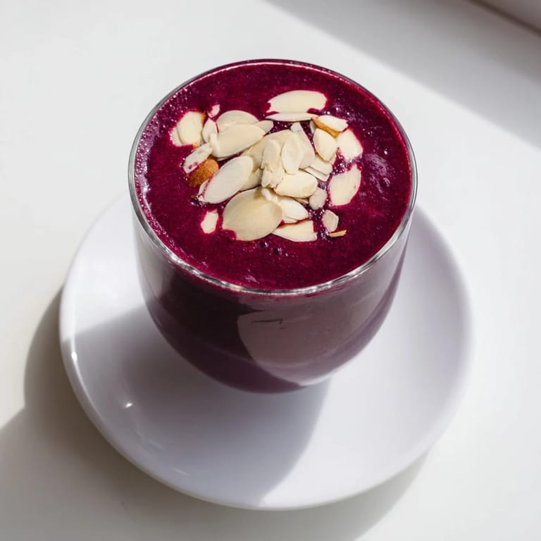 Two servings of vibrant Cherry Almond Smoothie beside a bowl of fresh cherries, a breakfast-ready blend with almond butter swirls.